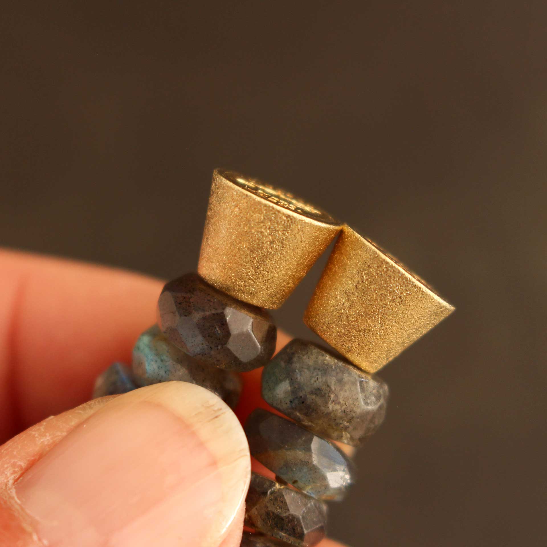 Geöffnete vergoldete Magnet-Kegelschließe eines Labradorit-Armbands, gehalten in den Händen. Sichtbar ist das starke Magnetinnenteil, das für sicheren Halt und einfaches Anlegen des handgefertigten Schmuckstücks sorgt.