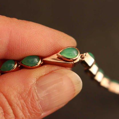 Makroansicht des handgefertigten, unsichtbar integrierten Kastenschlosses aus 750er Rotgold plattiertem 925 Silber, das sich nahtlos in die Reihe der gefassten Chrysoprastropfen einfügt. Gehalten in den Fingern.