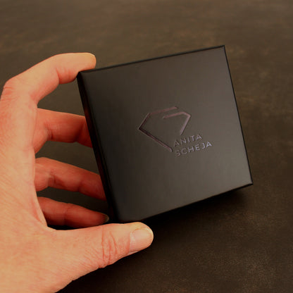 Hochwertige schwarze Schmuckschachtel mit eleganter, schwarzer Logo-Prägung für die sichere und stilvolle Aufbewahrung des Schmuckstücks.