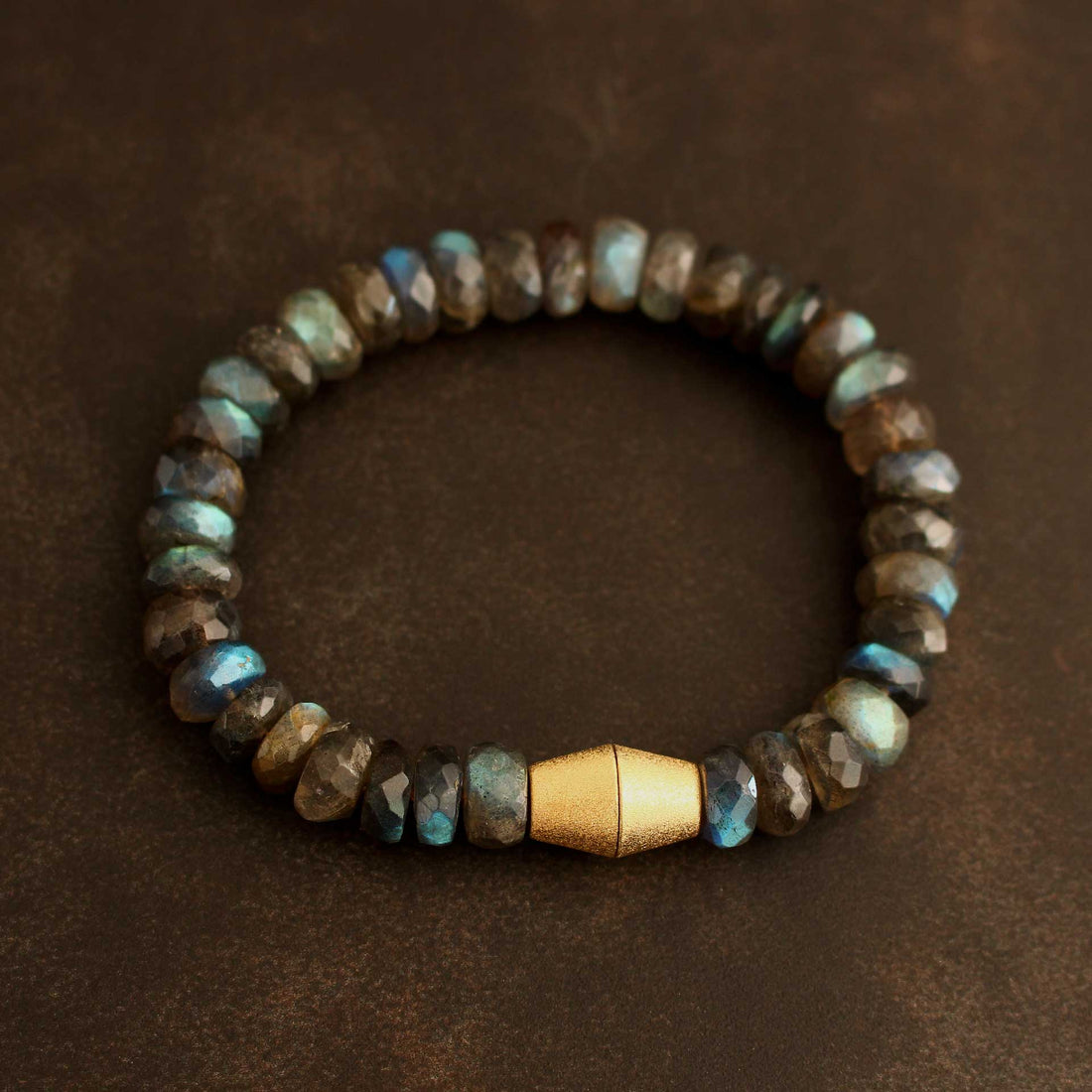 Handgefertigtes Edelstein-Armband aus der Goldschmiede-Werkstatt in Bayern: Facettierte Labradorit-Rondelle (10-12mm) mit magischem Blauschimmer und einer matt vergoldeten Kegel-Magnetschließe aus 925 Silber, liegend auf dunklem Hintergrund.
